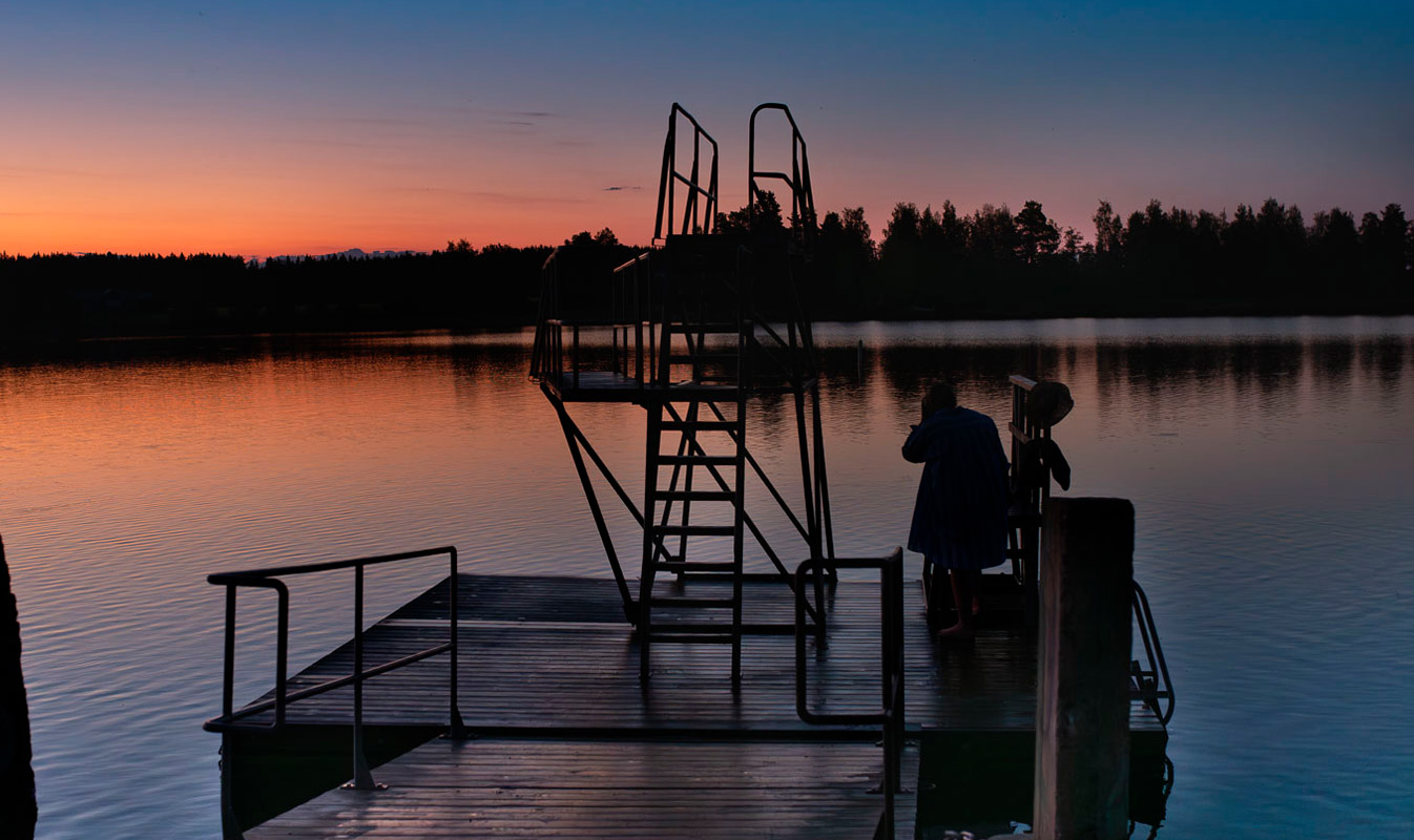 Lossin uimarannan hyppytorni piirtyy auringonlaskun oranssiksi värjäämälle taustalle.