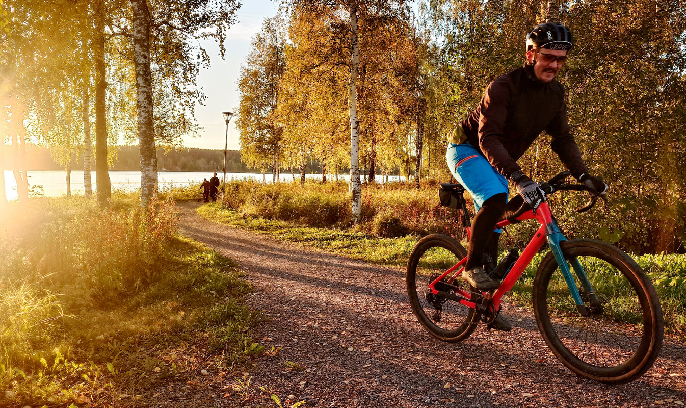 Henkilö pyöräilee rannalla auringon paistaessa takaa.