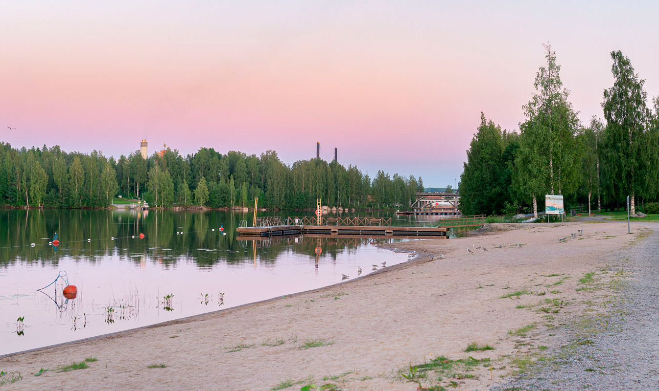 Äänejärven hiekkauimaranta, peilityyni järvi ja auringonlaskun violetiksi värjäämä taivas.