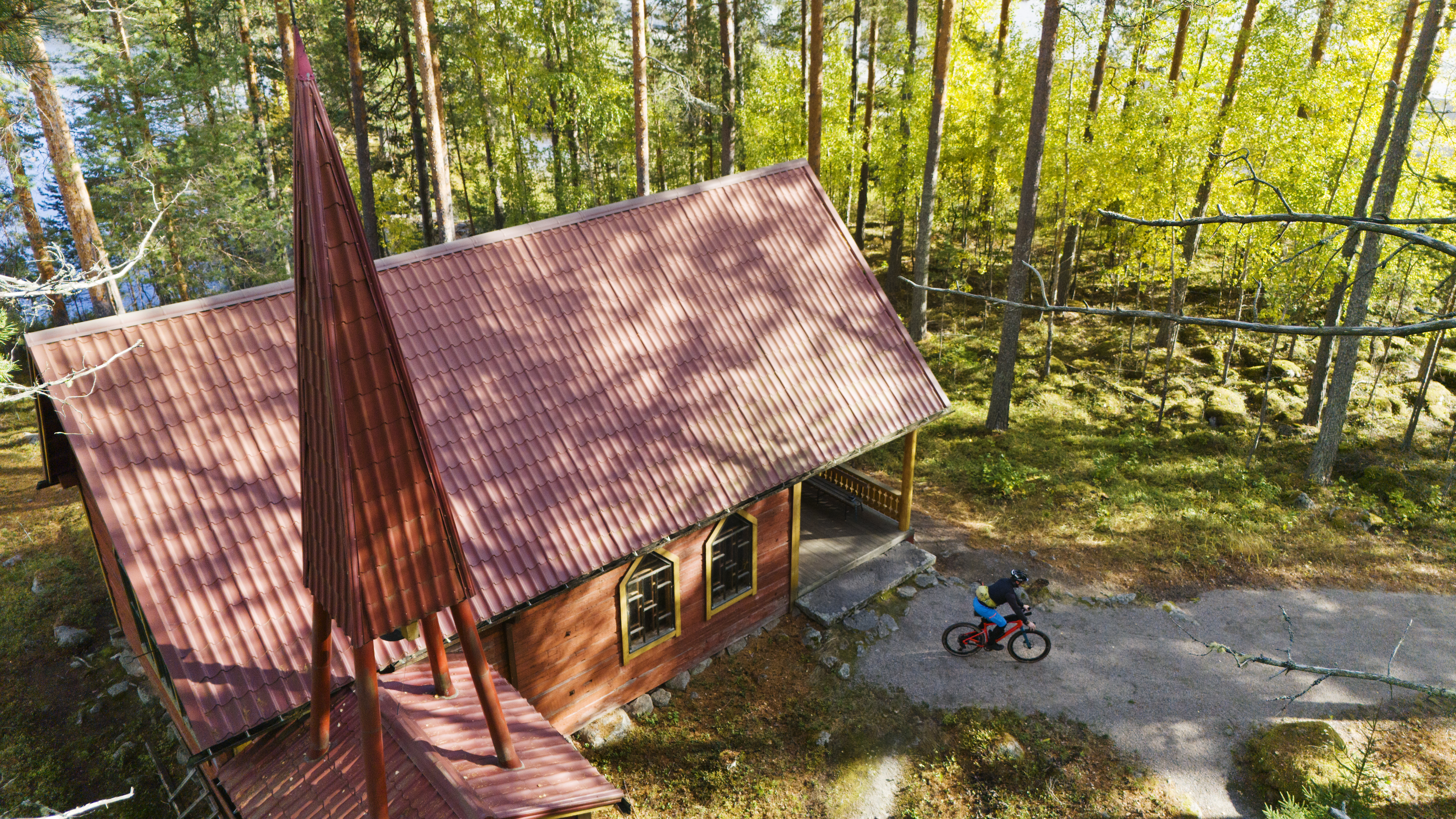 Kesäkirkko ylhäältä kuvattuna, pyöräilijä lähdössä polkemaan.
